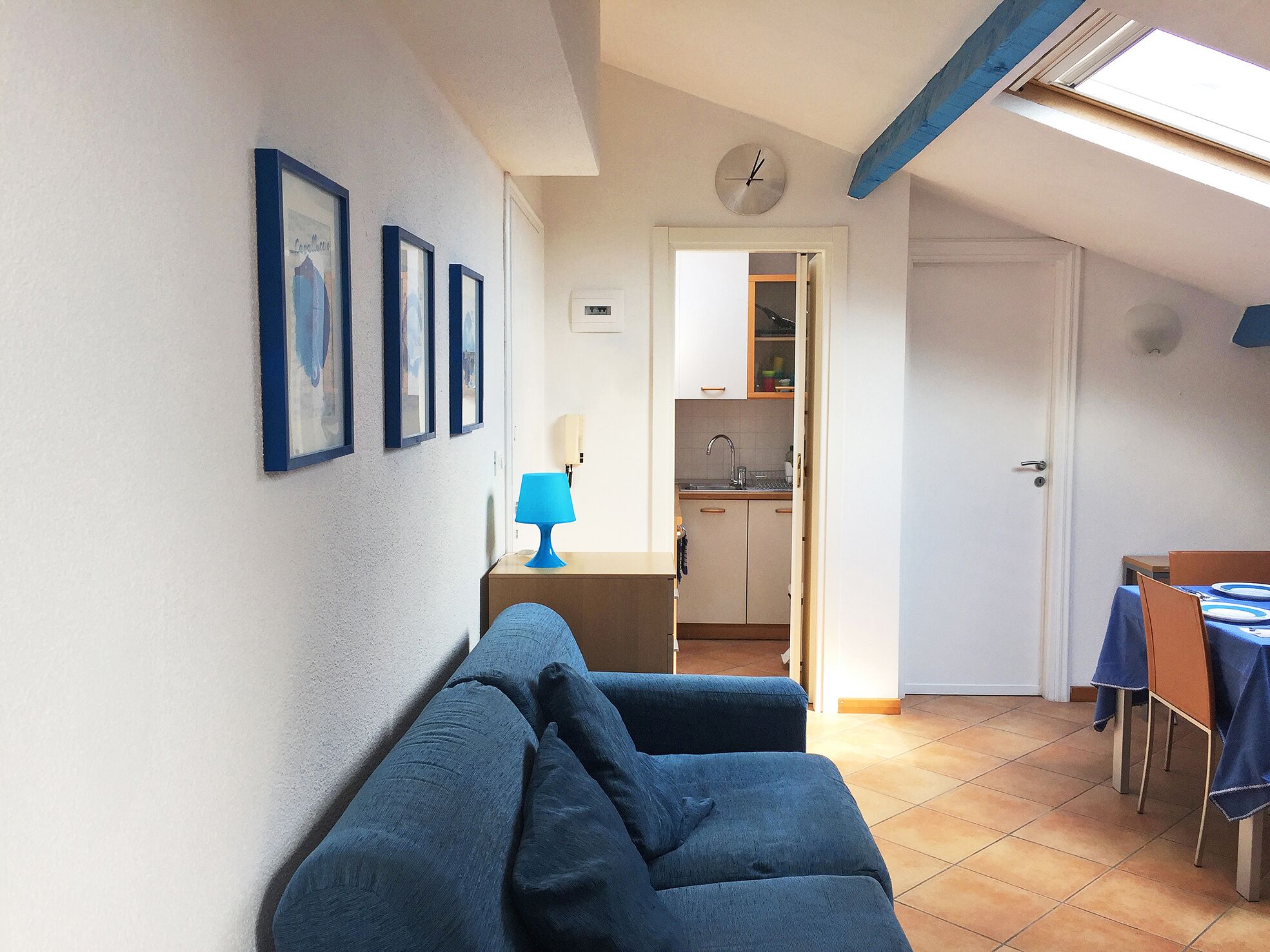 Un espacio habitable compacto con sofá, una mesa de comedor con platos, una zona de cocina y un reloj en la pared.