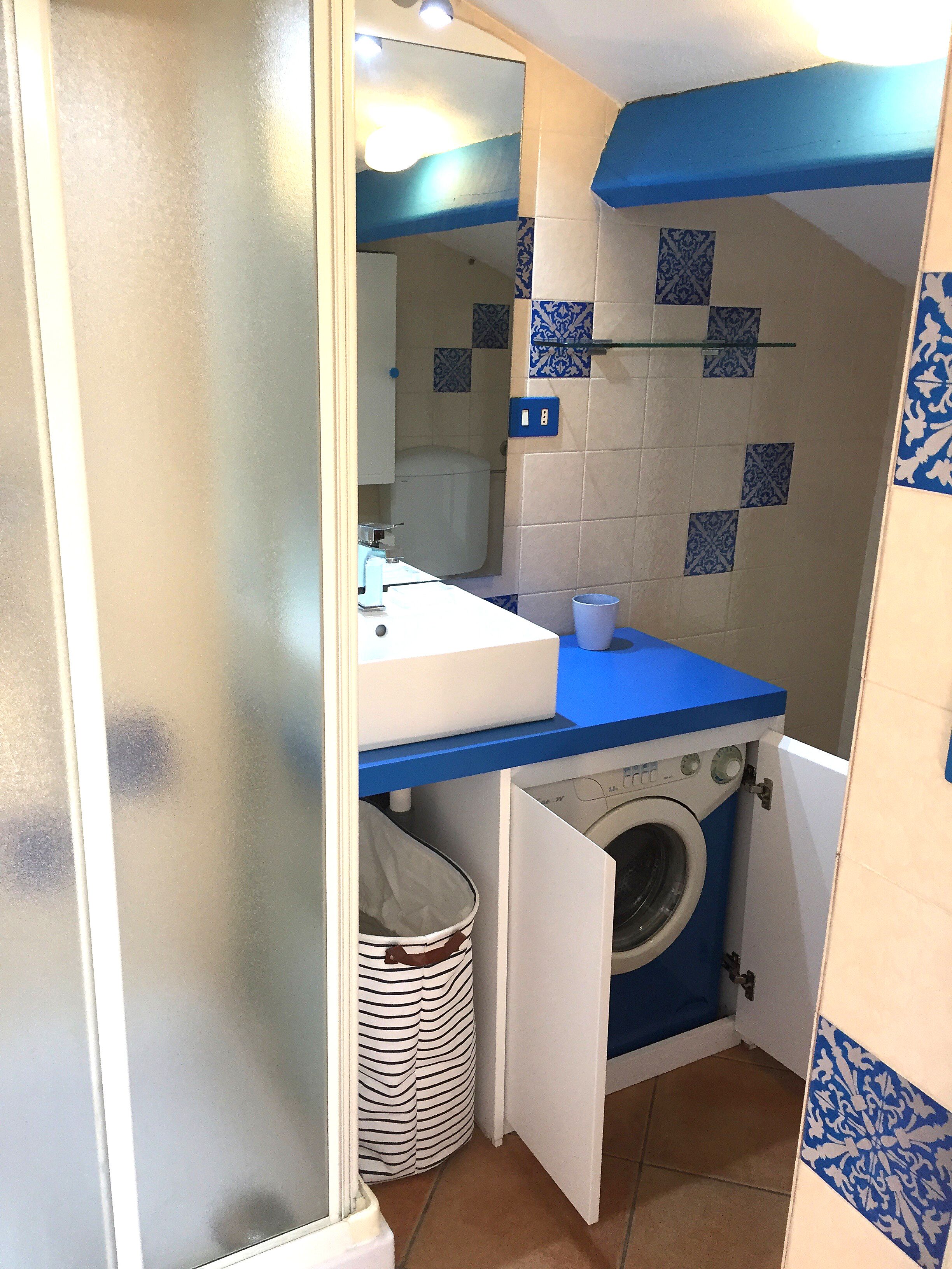 Een kleine badkamer met een wastafel, spiegel en wasmachine.
