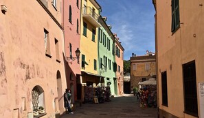 Une rue étroite bordée d’immeubles aux couleurs vives, un magasin sur le côté droit et une personne qui marche.