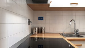 Eine moderne Küche mit weißen Fliesen, einer schwarzen Induktionskochplatte, Edelstahlgeräten und einer Holz Arbeitsplatte.