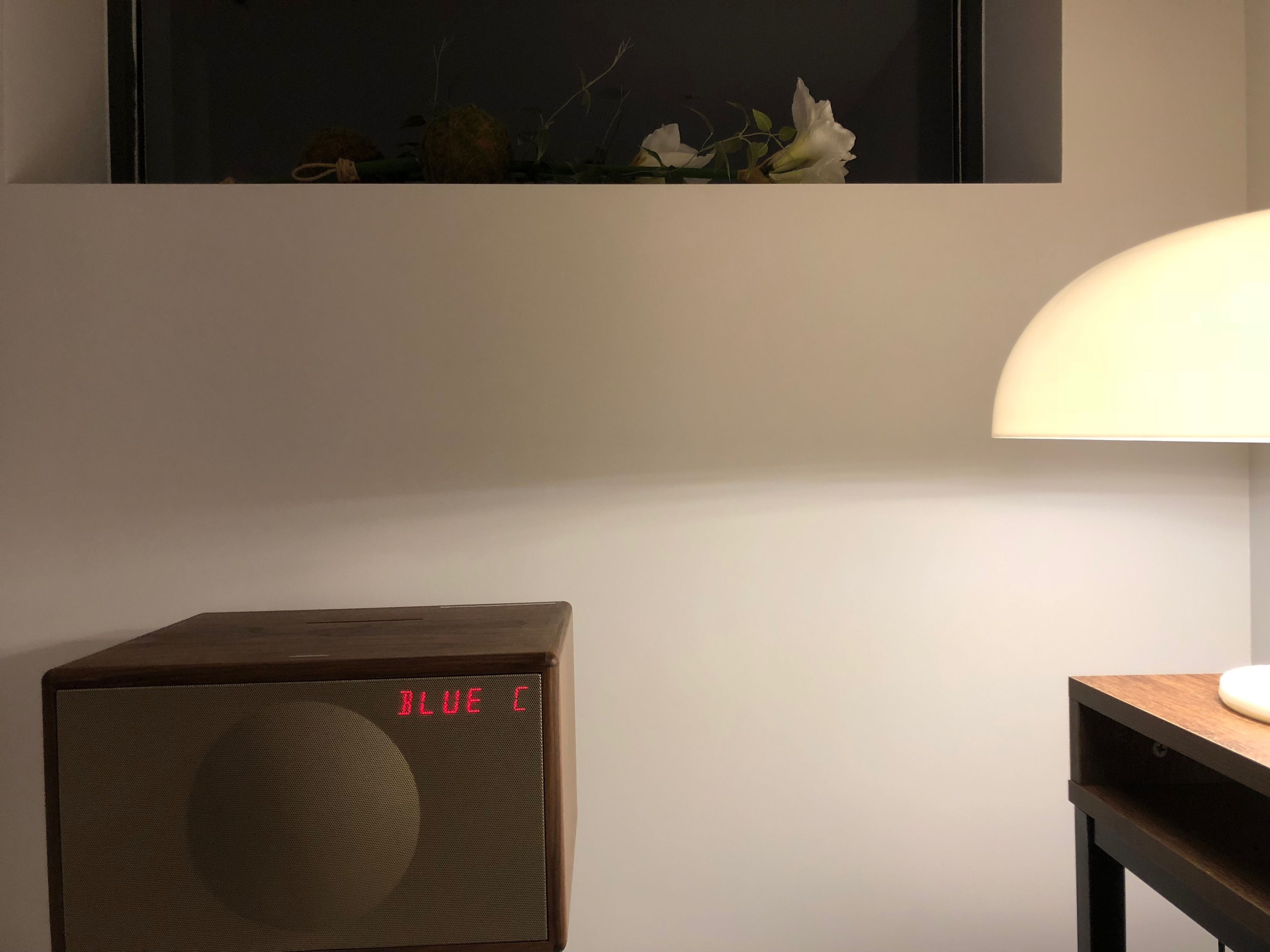 A room with a wooden speaker, a lamp, and a wall-mounted artwork.