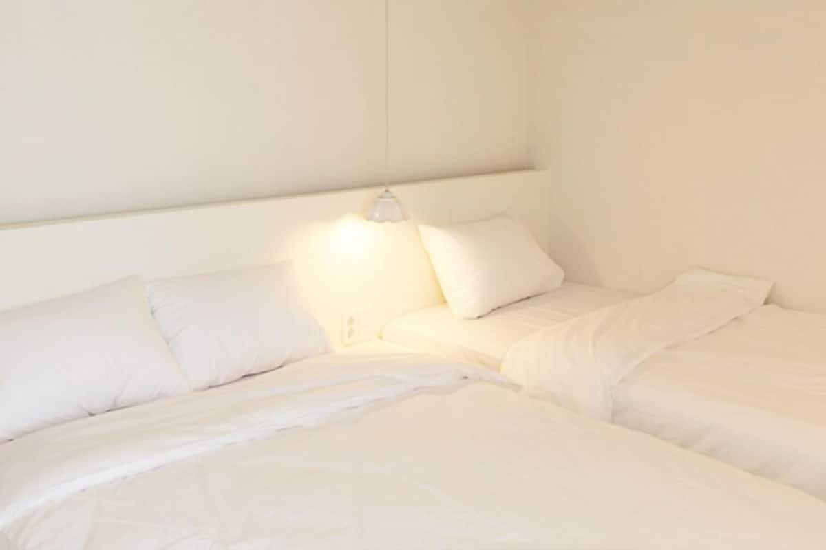 A bedroom with two beds, white bedding, and a bedside lamp.