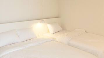 Une chambre avec deux lits, du linge de lit blanc et une lampe de chevet.