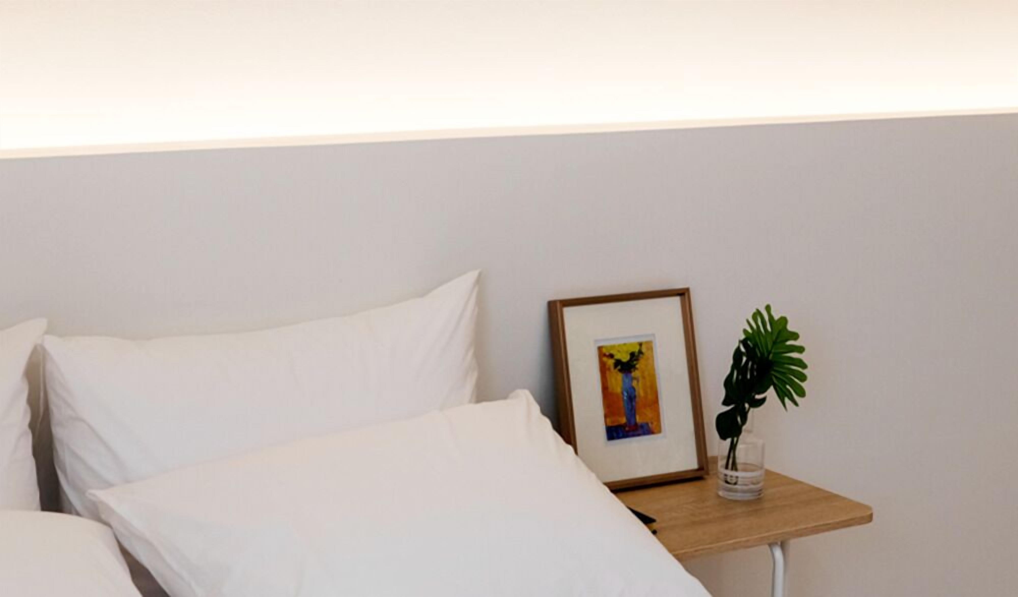 A neatly made bed with white linens and a small bedside table with a framed picture and a potted plant.