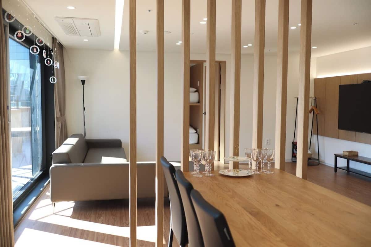 A modern living room with a sofa, a dining table with glassware, and a TV mounted on the wall.