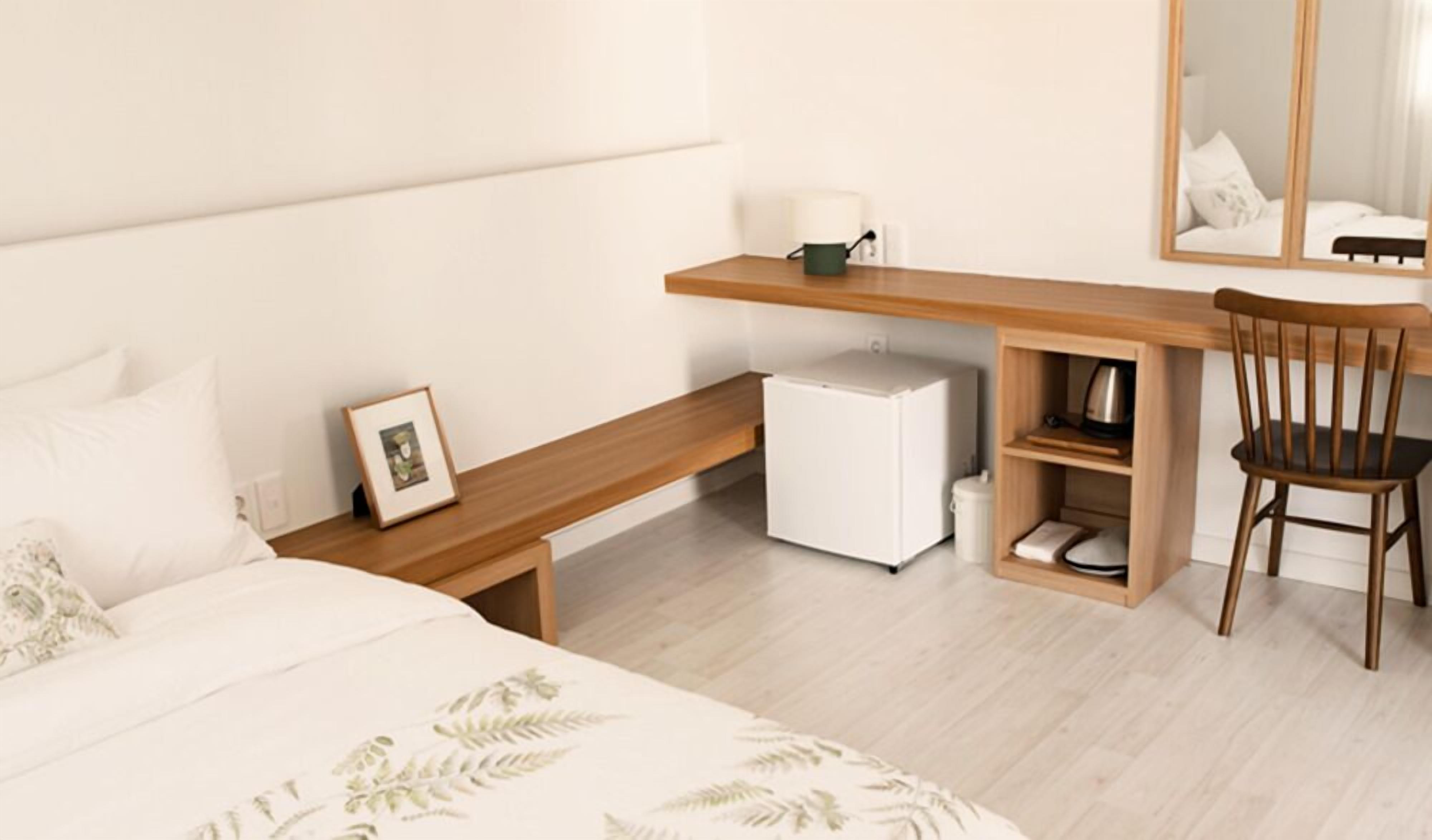 Une chambre à coucher comprenant un lit, un bureau avec une chaise, un petit réfrigérateur, une étagère avec une lampe et un tableau encadré.