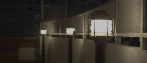 A row of outdoor wall-mounted lights along a white railing, with a building in the background.