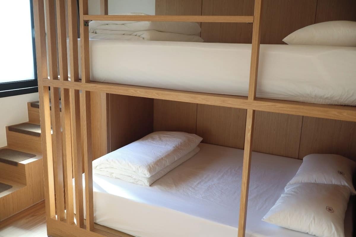 A bunk bed with a wooden frame, white bedding, and a staircase to the left.