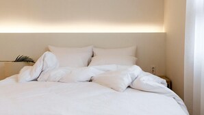 Un lit bien fait, avec du linge de lit blanc et des oreillers, une lampe de chevet et une prise électrique sur le mur.