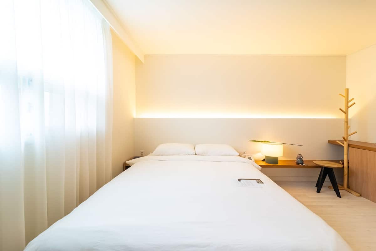 A hotel room with a large bed, bedside tables, a lamp, and a wooden decor piece.