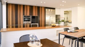 Une cuisine moderne avec un mur d’accent en bois, des appareils en acier inoxydable et un coin repas comprenant une table et des chaises en bois.