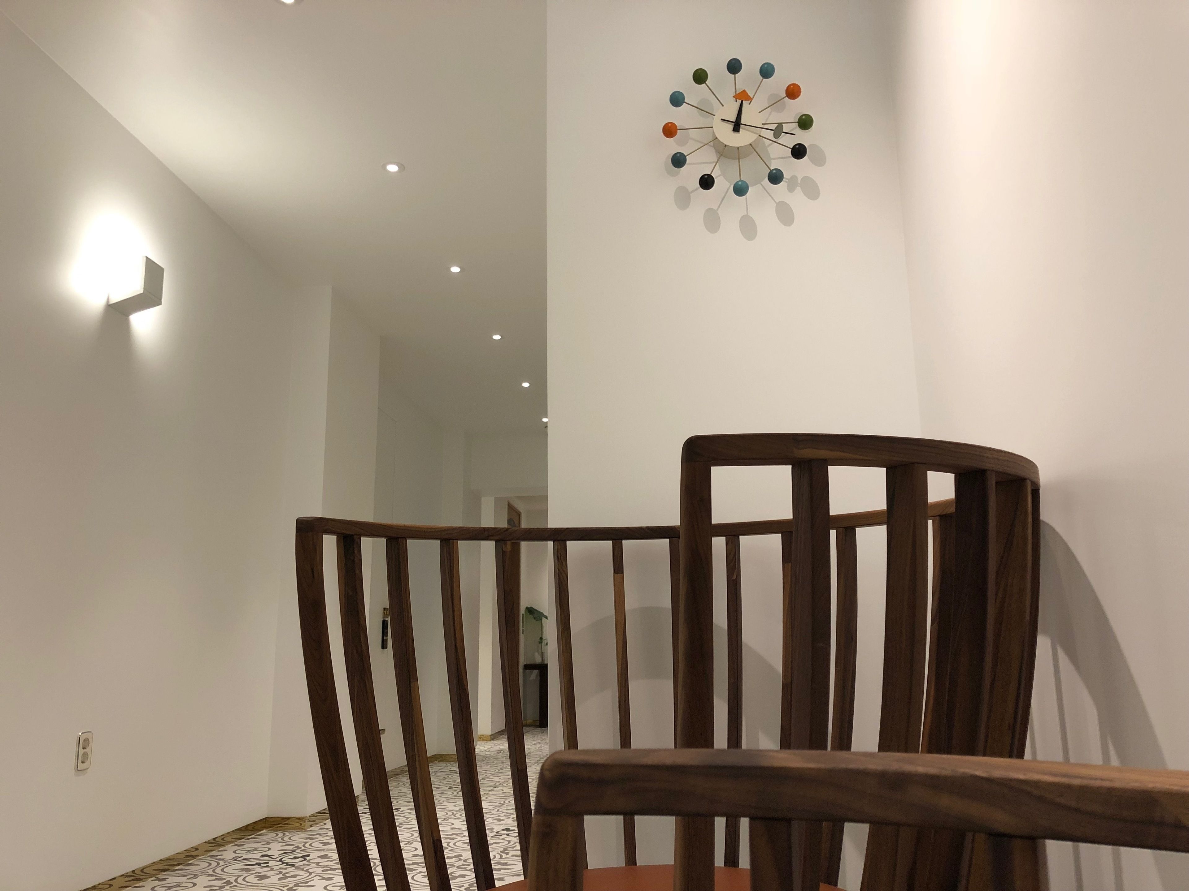 A wooden chair in a room with a modern clock on the wall.
