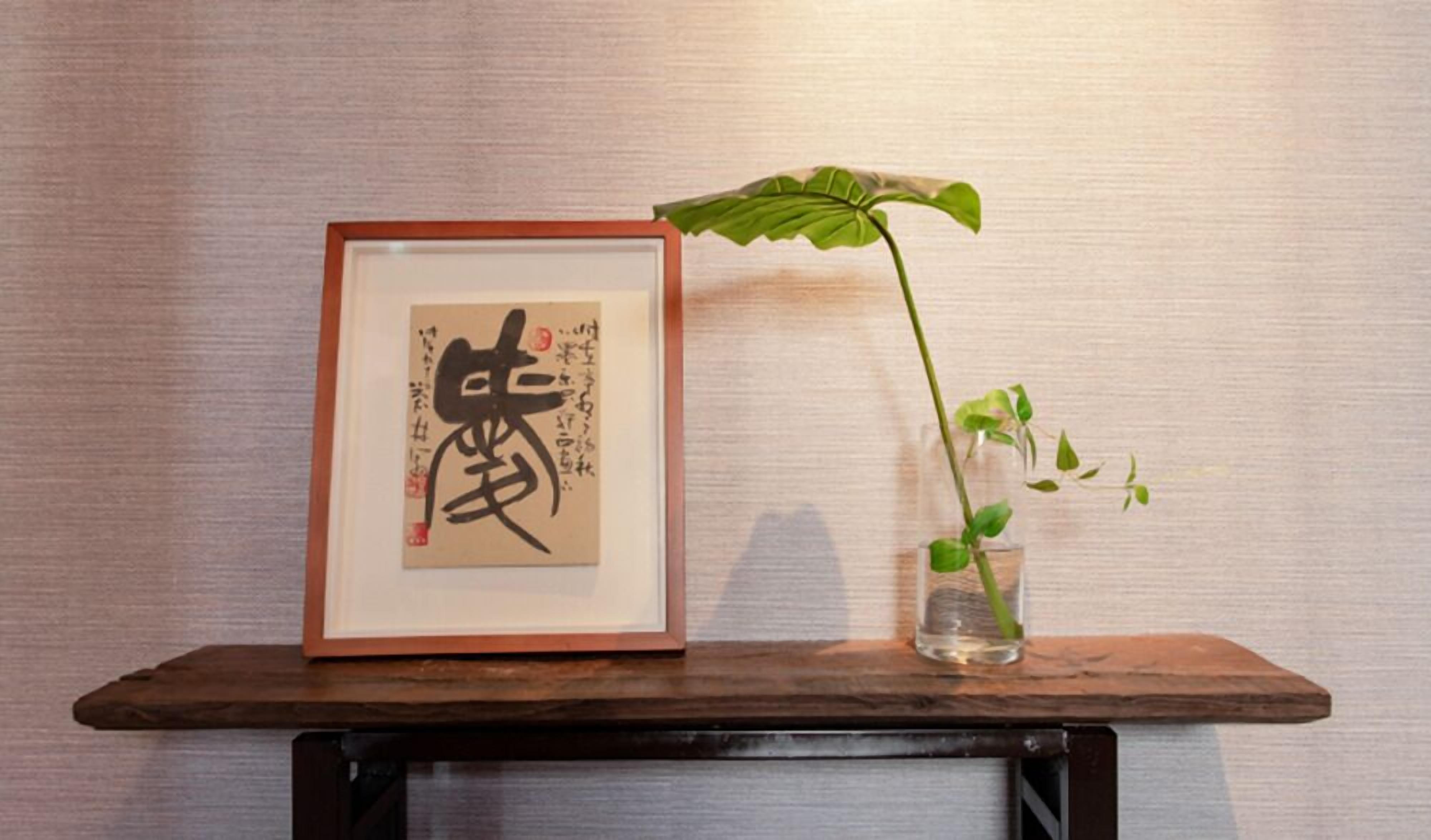 A framed calligraphy piece on a wooden shelf with a potted plant beside it.