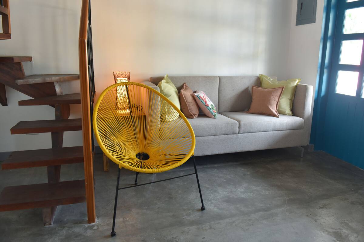 A room with a grey sofa, yellow chair, wooden staircase, and a blue wall.