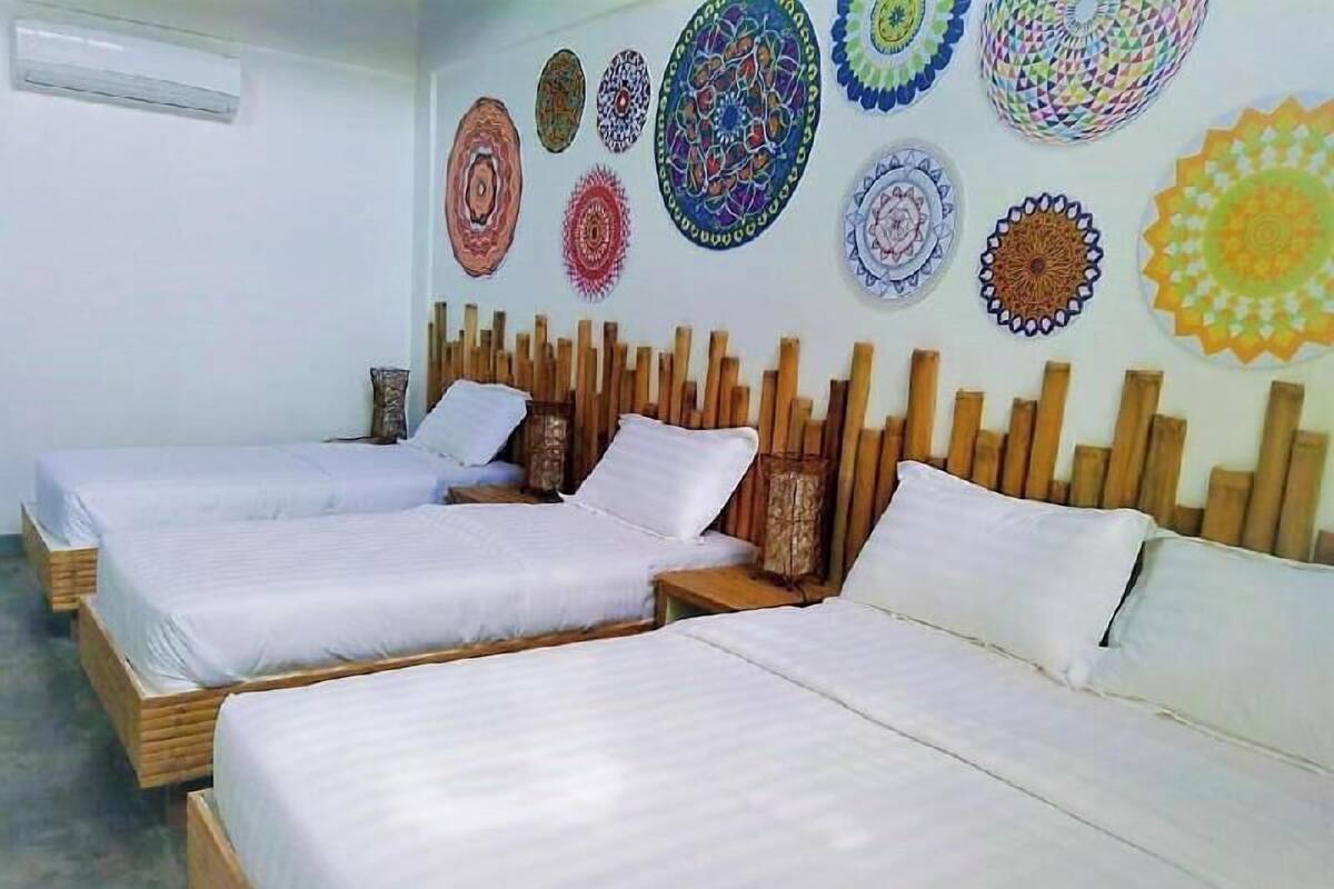 A room with three beds, a wooden headboard, and a wall decorated with colorful circular patterns.