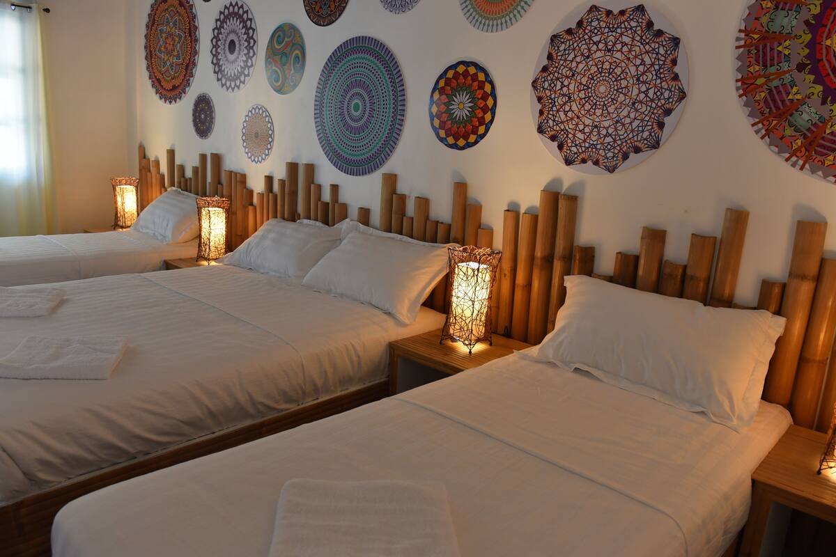 A hotel room with two beds, each with white linens and pillows, and a bedside table with a lamp. The walls are decorated with colorful, circular wall art.