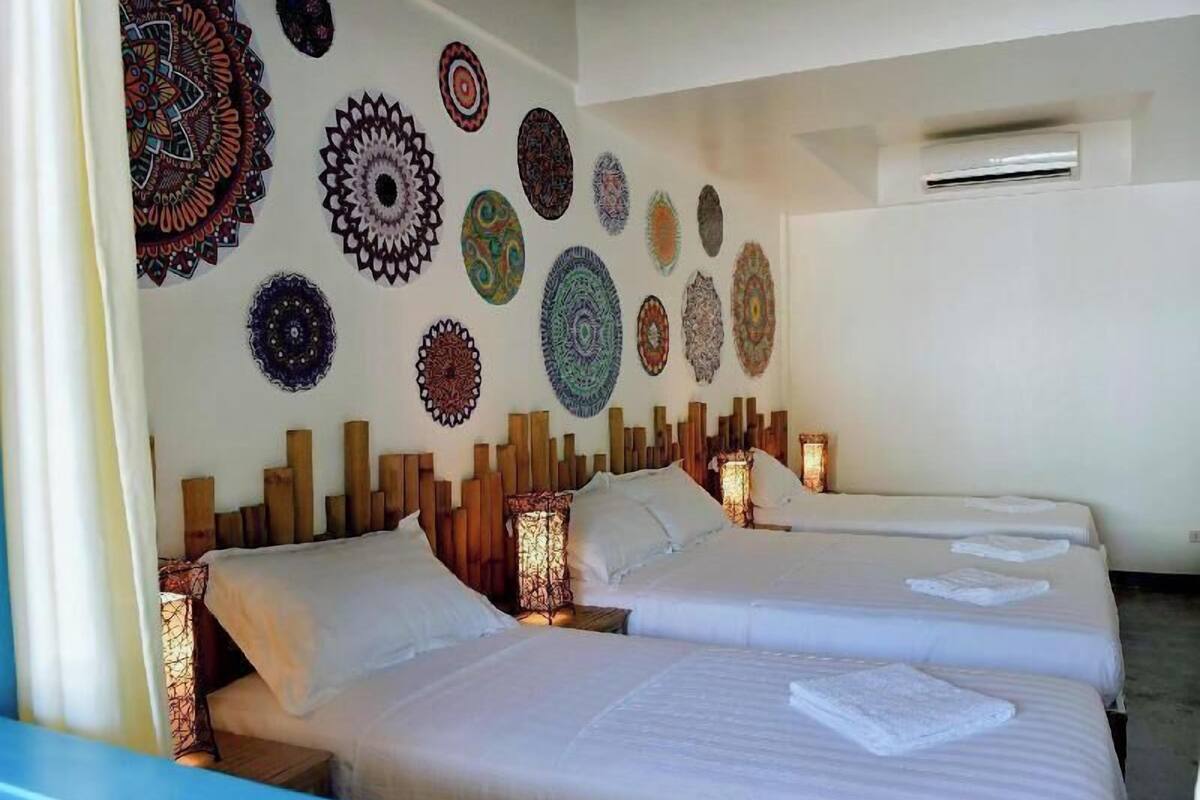 A hotel room with two beds, a wall decorated with circular patterns, and an air conditioning unit.