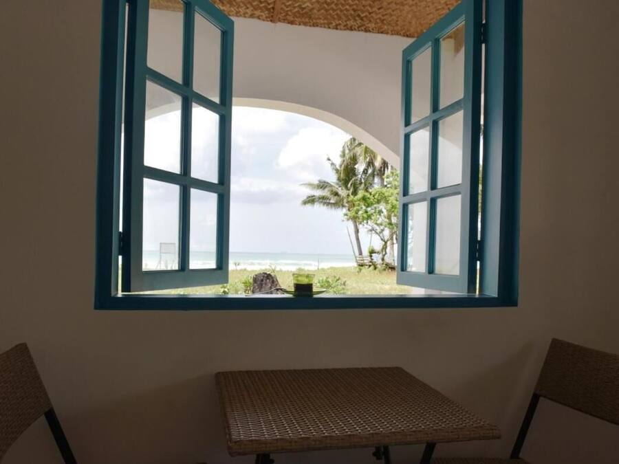Ein Zimmer mit Blick auf den Strand durch ein Fenster mit blauen Rahmen.
