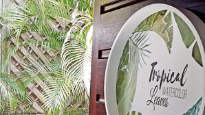 Pared de madera con un letrero circular que presenta hojas de acuarela tropicales y el texto 'Tropical Watercolor Leaves'.
