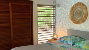 Un dormitorio con una cama, un ventanal con persianas, un equipo de aire acondicionado y un adorno de pared tejido.