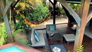 Una terraza de madera con piscina, mobiliario exterior y una hamaca.