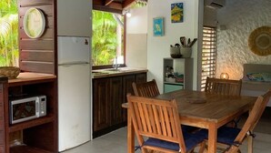 Una cocina con armarios de madera, una mesa de comedor con sillas, una lámpara colgante y un refrigerador.