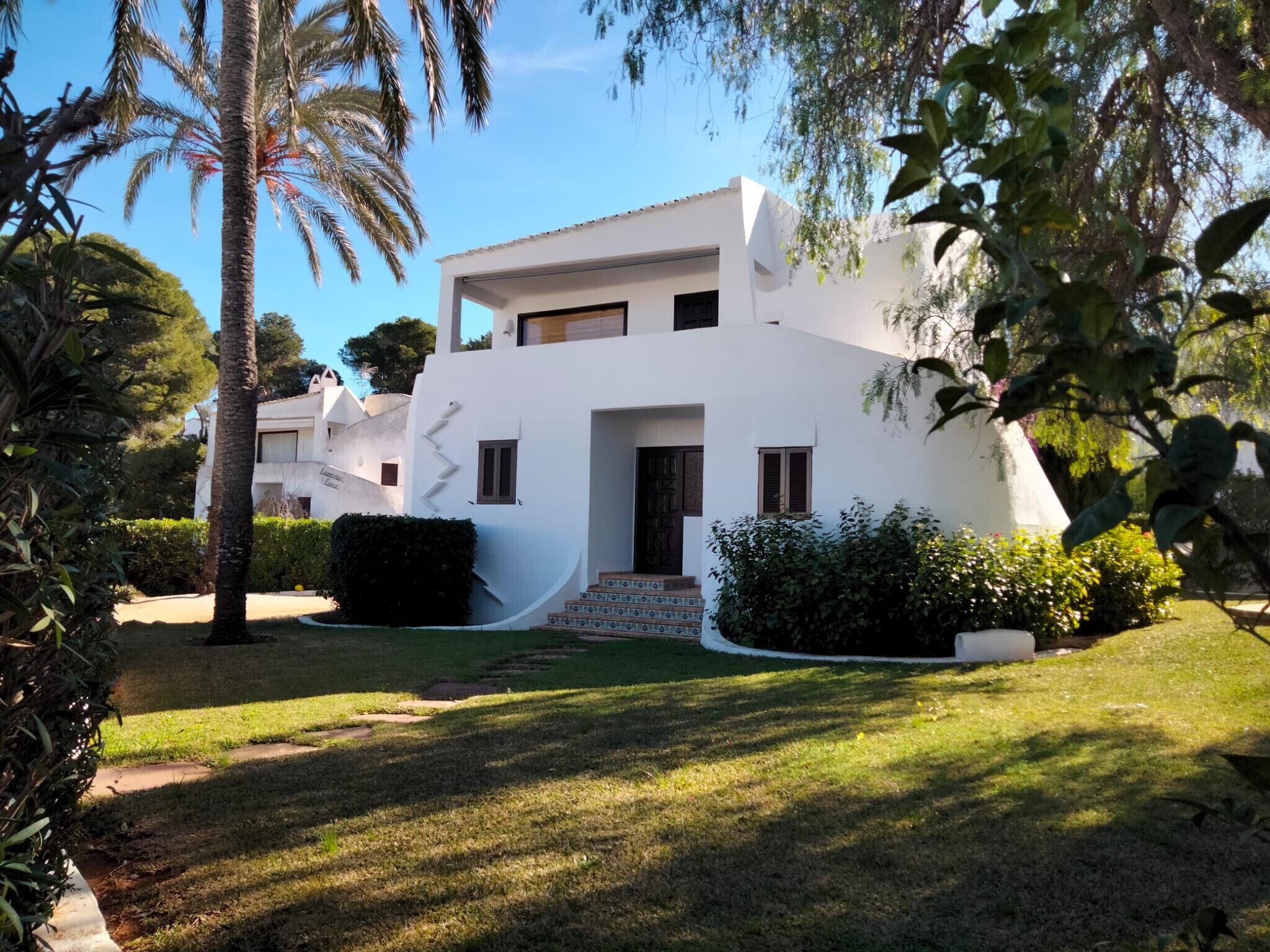 A modern white building with a flat roof, a small entrance, and a staircase leading to the main door.