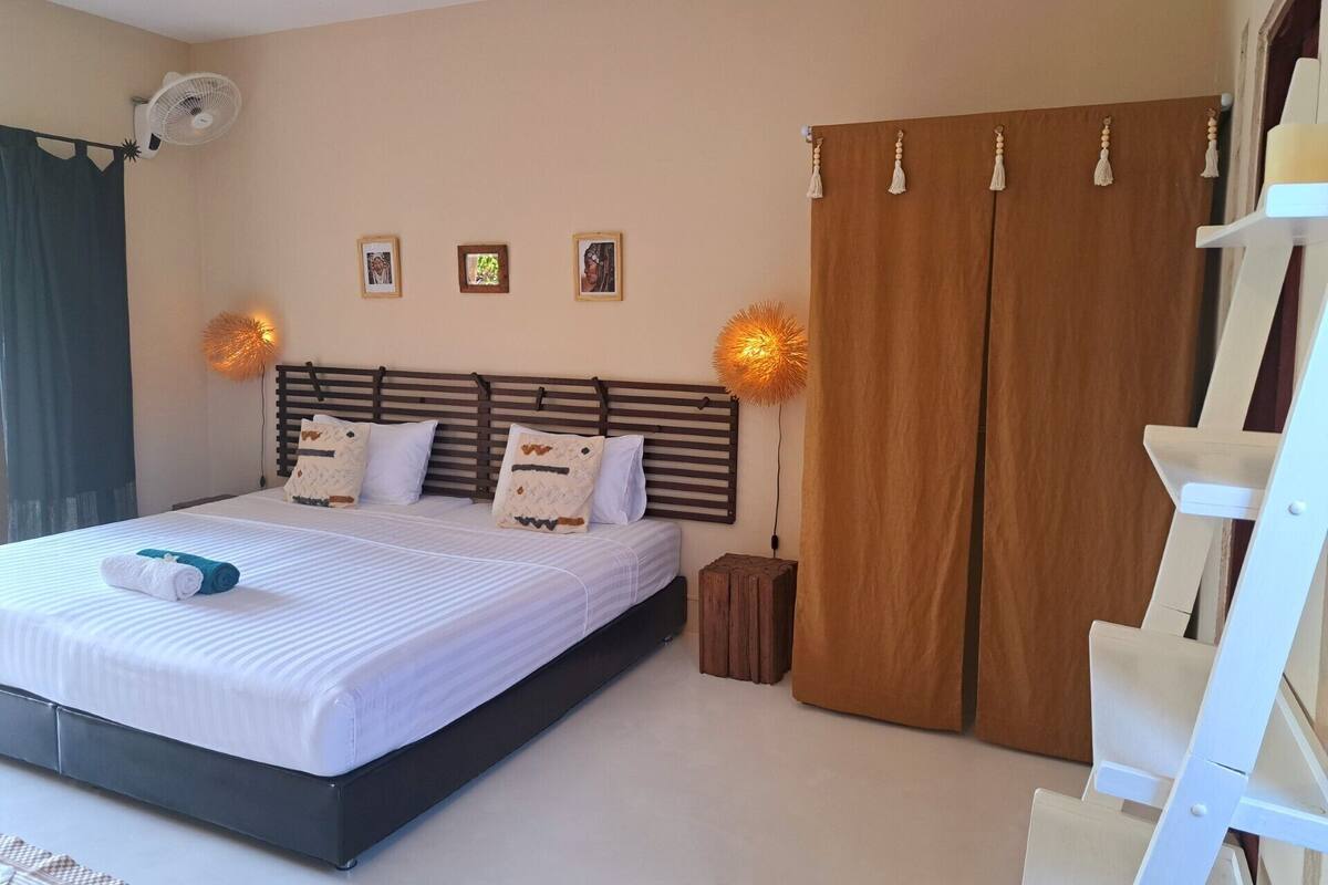 A bedroom with a bed, bedside lamps, a wardrobe, and a fan.