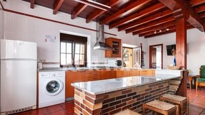 A kitchen with a central island, wooden cabinets, a washing machine, and a tiled floor. - Apto Tapia 2 - rural apartment in Luces (Colunga), Northern Spain | 6 guests (San Telmo)