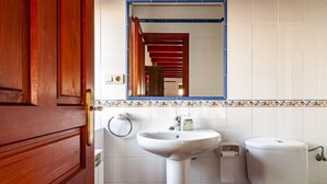 A bathroom with a wooden door, a white sink, a toilet, and a mirror above the sink. - Apto Tapia 2 - rural apartment in Luces (Colunga), Northern Spain | 6 guests (San Telmo)
