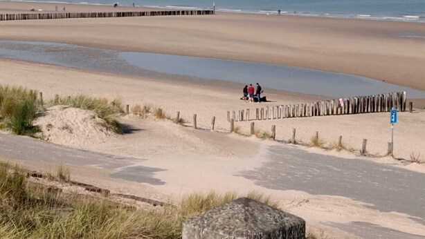 A beach with a wooden walkway, a sandy path, and a few people walking.