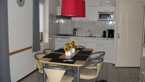 A compact kitchen with a dining area, including a table with chairs, a red hanging light, and a clock on the wall.