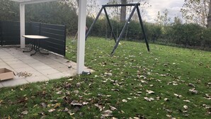 A covered patio area with a swing set, a table, and a chair.