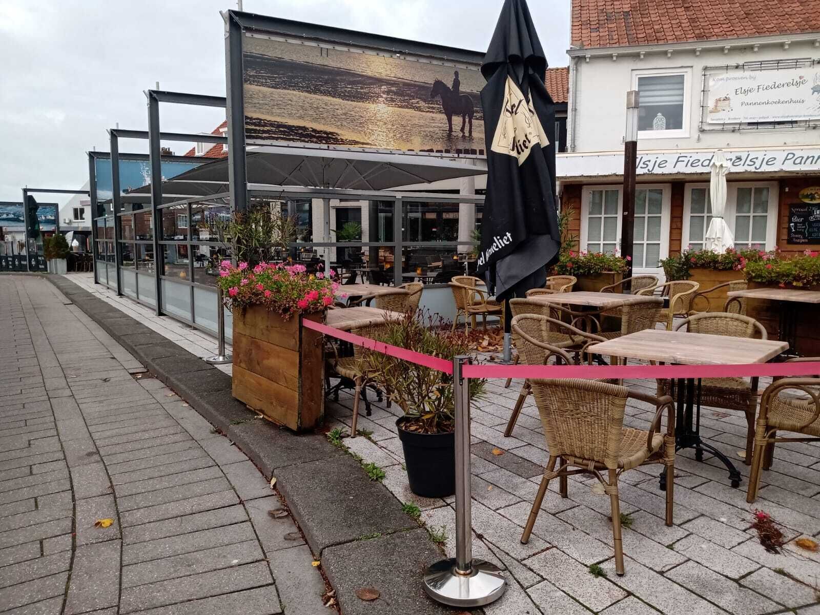 An outdoor cafe with wicker chairs and tables, a planter with flowers, and a banner advertising a local bakery.