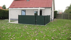 A house with a red tiled roof, a white exterior, and a green fence.
