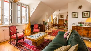 Un salon chaleureux avec un canapé vert, un tapis aux motifs rouges et bleus, une table basse en bois et un fauteuil rouge.