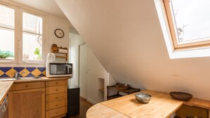 Une cuisine avec des meubles de rangement en bois, un four à micro-ondes, un évier et une fenêtre avec une horloge.