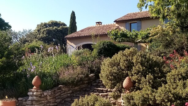 Un jardin avec des murs en pierre, des plantes en pot et une maison avec un toit en tuiles.