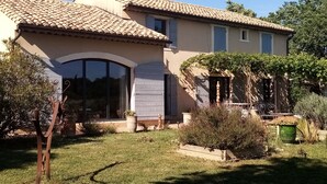 Une maison à deux étages, avec un toit recouvert de tuiles, une grande fenêtre en arc de cercle et un petit porche avec une chaise.