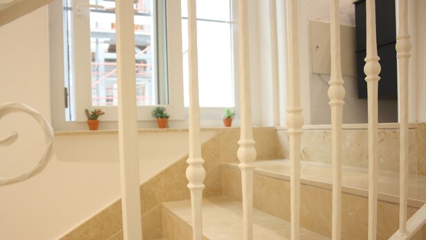 A staircase with white balusters and beige steps, leading to a landing with a window and potted plants. - Luxurious relaxation in town! (Napoli)
