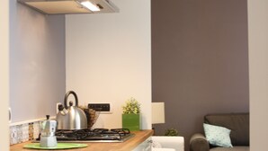 A narrow kitchen with a wooden countertop, white cabinets, and a stove. A small table with a plant and a lamp is visible in the background. - Luxurious relaxation in town! (Napoli)