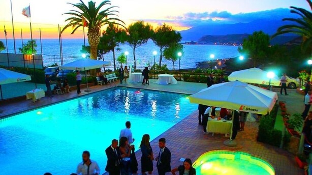 Zona de piscina con vistas al atardecer, mobiliario exterior y sombrillas.