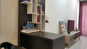 A reception area with a dark reception desk, a shelf with books and a vase, a tray with bottled water and a small plant, and a signboard. - Stay Awhile at Aeropod Sovo Studio (Kota Kinabalu)