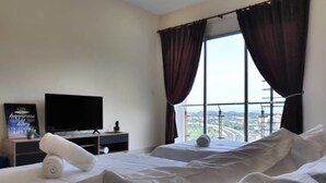 A hotel room with two beds, a TV, and a view of a cityscape through large windows. - Stay Awhile at Aeropod Sovo Studio (Kota Kinabalu)