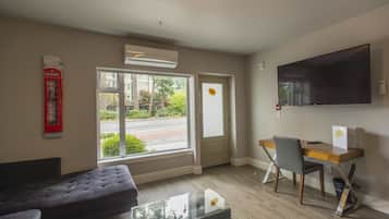 Une chambre moderne équipée d’un canapé, d’une table basse en verre, d’un bureau avec une chaise, d’un téléviseur à écran plat et d’une grande fenêtre donnant sur la rue.