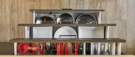 A kitchen with a wooden wall background, a stainless steel countertop, and a variety of kitchen utensils and cookware.