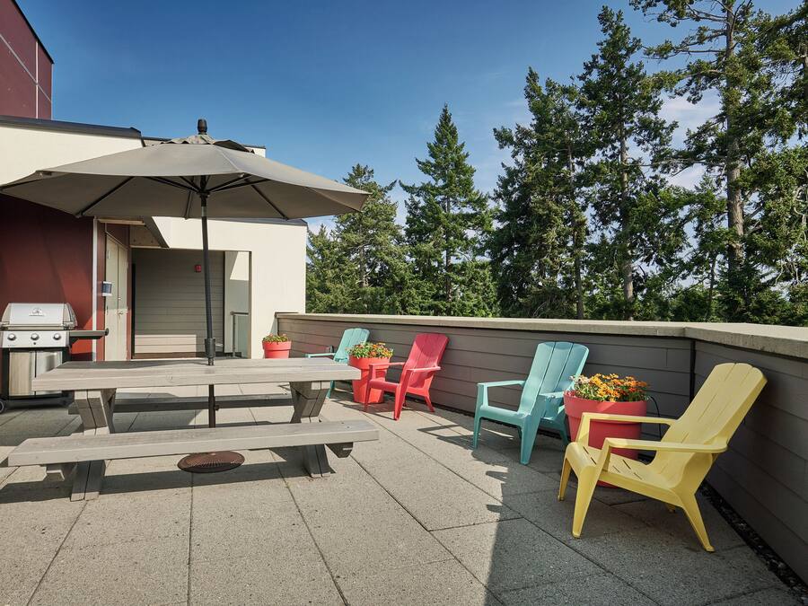 Un patio al aire libre con mesa de picnic, sillas, una parrilla y plantas en macetas.