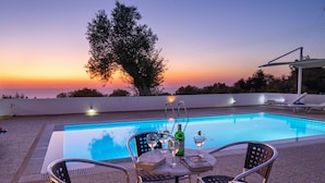 A poolside setting with a table, chairs, and a bottle of champagne.