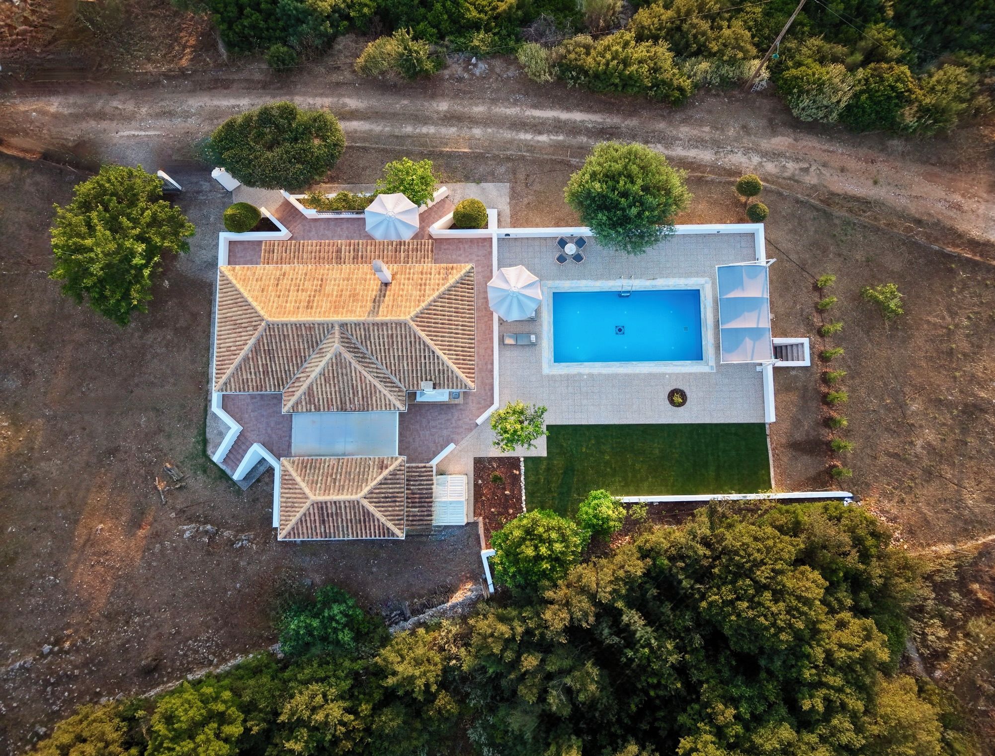 An aerial view of a property with a swimming pool, patio area, and a large lawn.