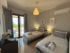 A hotel room with two beds, a desk, a chair, a window with curtains, and a ceiling light.